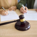 Casal assinando documentos com martelo de juiz em primeiro plano